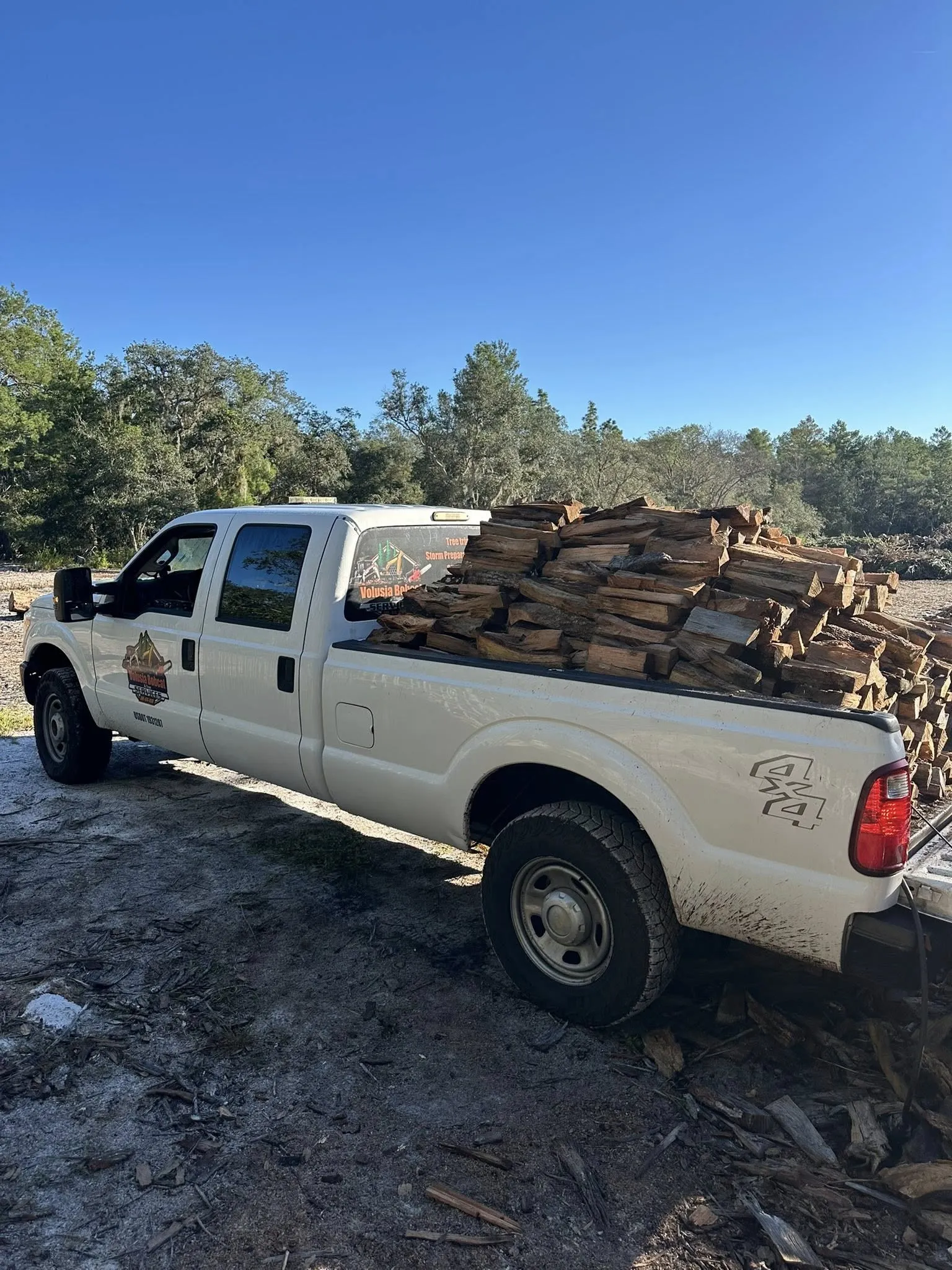 White 4x4 pickup truck loaded with seasoned firewood, ready for delivery